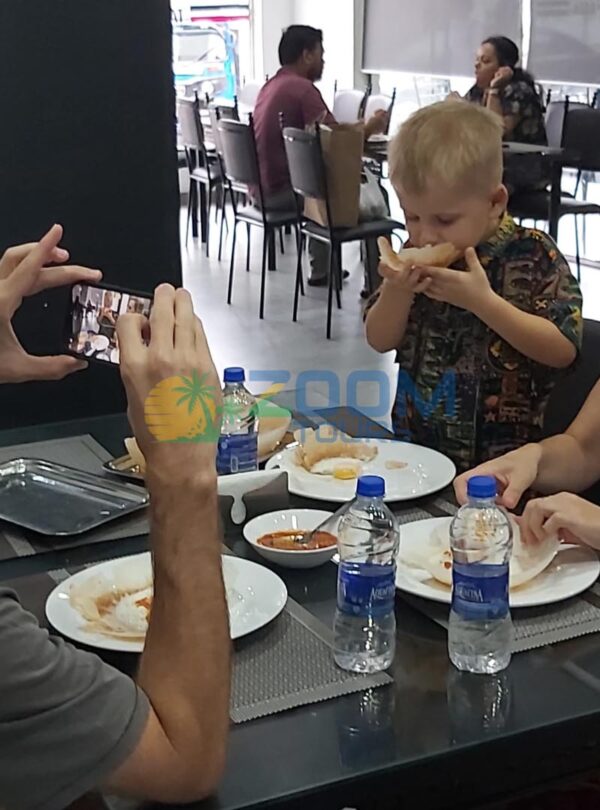 A young couple with a child enjoying egg hoppers at a Colombo street food stall while the father captures a photo of his son taking a bite.